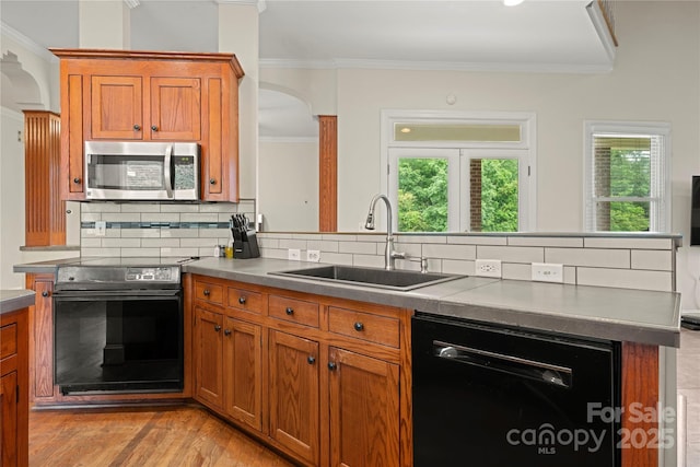 kitchen with black appliances, a sink, arched walkways, ornamental molding, and brown cabinetry