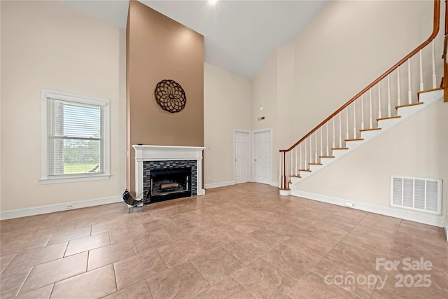 unfurnished living room with high vaulted ceiling, a tiled fireplace, stairs, and baseboards