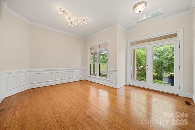 spare room featuring light wood-type flooring, ornamental molding, rail lighting, and a wainscoted wall