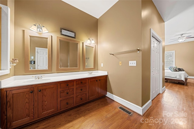bathroom with wood finished floors, baseboards, double vanity, ceiling fan, and ensuite bathroom