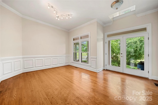 spare room featuring light wood-type flooring, track lighting, crown molding, and wainscoting