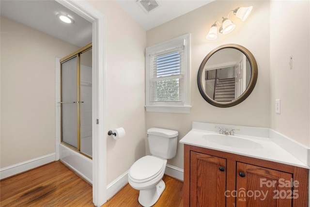 bathroom featuring wood finished floors, toilet, vanity, baseboards, and enclosed tub / shower combo