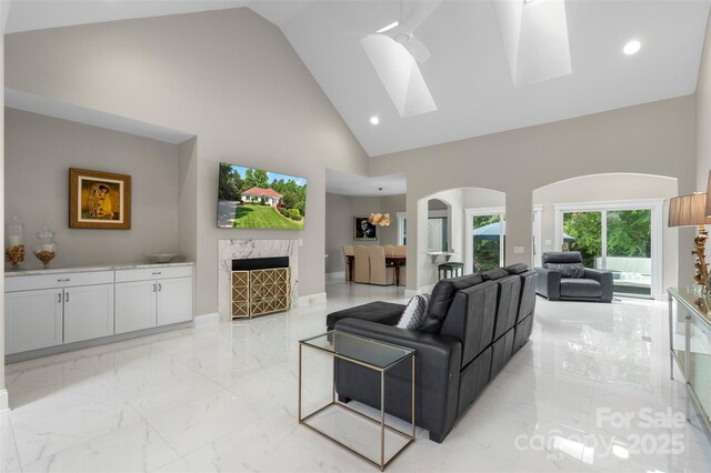 living room with arched walkways, high vaulted ceiling, light marble finish floors, a skylight, and recessed lighting