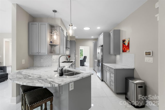 kitchen with gray cabinets, a sink, a peninsula, stainless steel refrigerator, and backsplash