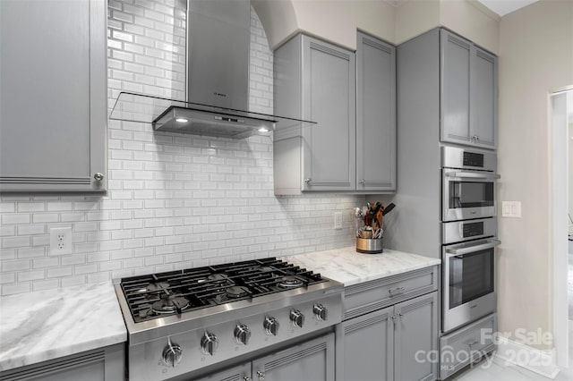 kitchen with wall chimney range hood, gray cabinets, appliances with stainless steel finishes, and tasteful backsplash