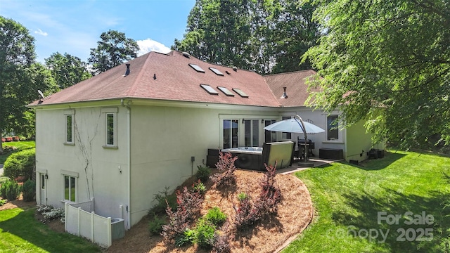 back of property with stucco siding, a lawn, roof with shingles, and a patio