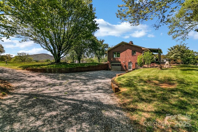 view of home's exterior with aphalt driveway, a chimney, brick siding, an attached garage, and a yard