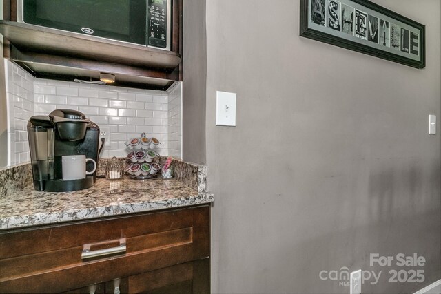 interior space with stainless steel microwave, light stone countertops, and decorative backsplash