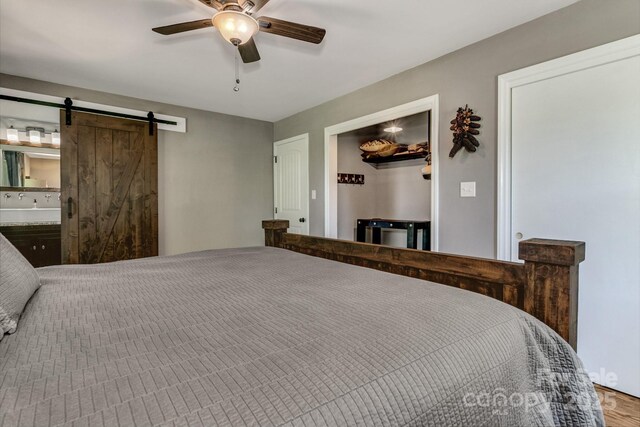 bedroom with connected bathroom, a ceiling fan, a barn door, and wood finished floors
