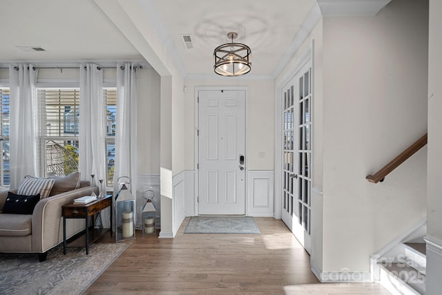 entryway with wood finished floors, a wainscoted wall, ornamental molding, stairs, and a decorative wall