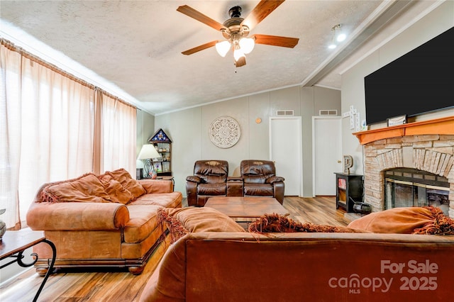 living area featuring a textured ceiling, lofted ceiling with beams, a glass covered fireplace, wood finished floors, and a ceiling fan