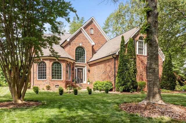 traditional-style house featuring roof with shingles, a front yard, and brick siding