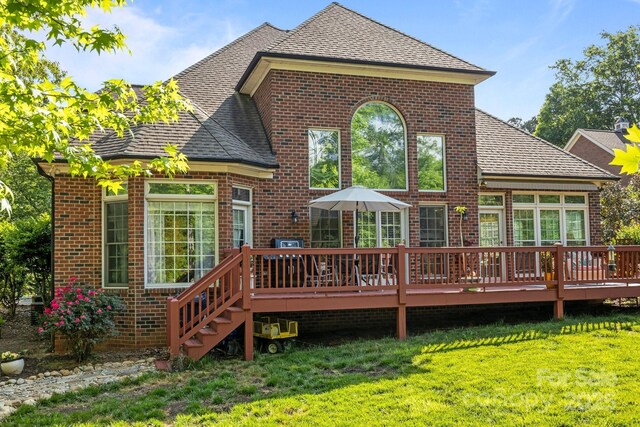 rear view of property featuring a lawn, brick siding, and a deck