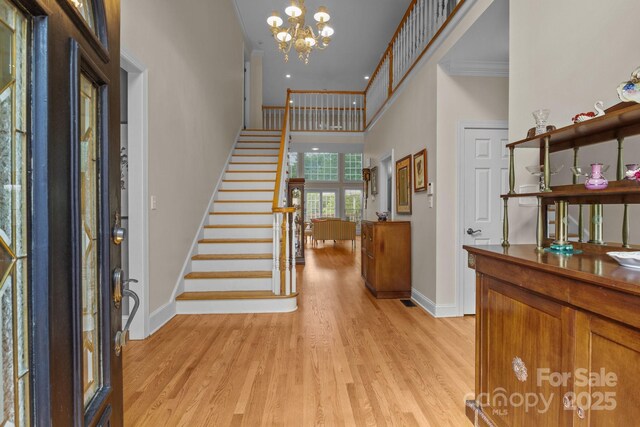 entryway featuring crown molding, light wood-type flooring, baseboards, an inviting chandelier, and stairs