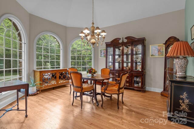 dining area with baseboards, an inviting chandelier, vaulted ceiling, and light wood-type flooring