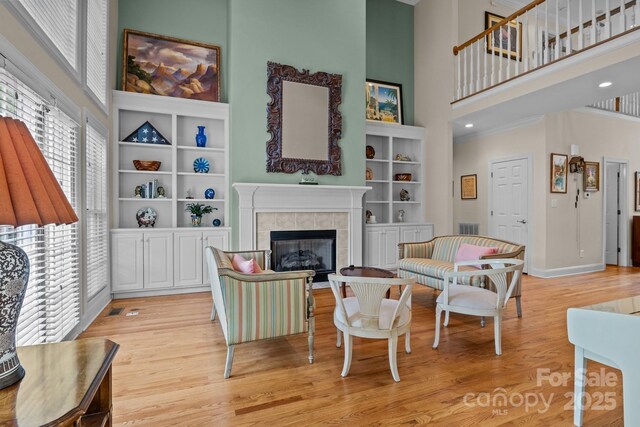 living room featuring visible vents, a towering ceiling, a tile fireplace, baseboards, and light wood finished floors