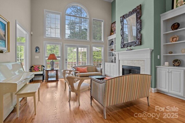 living room featuring built in features, a high ceiling, light wood finished floors, and a tile fireplace
