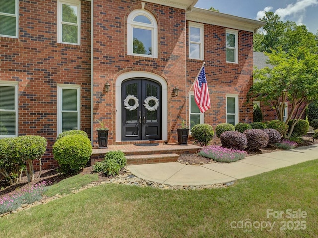 doorway to property with brick siding, french doors, and a lawn