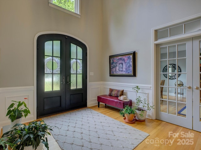 doorway to outside with arched walkways, wood finished floors, a wainscoted wall, and french doors