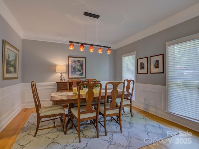 dining area featuring light wood-type flooring, a wainscoted wall, and ornamental molding