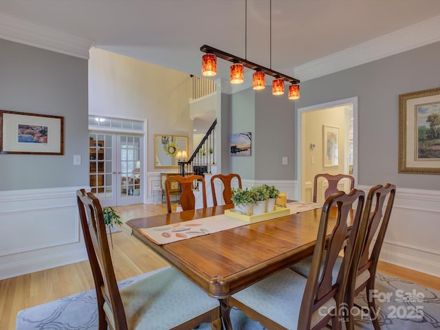 dining room featuring a decorative wall, ornamental molding, stairs, and light wood-style flooring