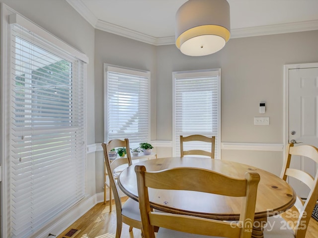 dining room featuring light wood-type flooring, visible vents, a wainscoted wall, and ornamental molding