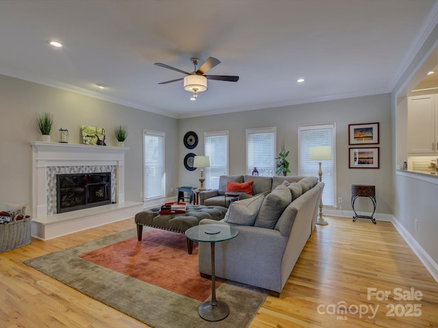 living area with light wood finished floors, a high end fireplace, a ceiling fan, crown molding, and baseboards