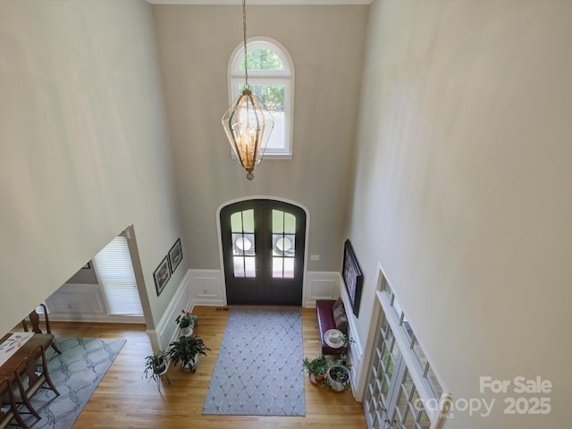 foyer featuring wood finished floors, arched walkways, an inviting chandelier, french doors, and a high ceiling