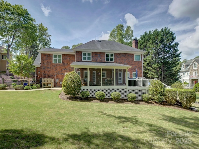 rear view of property with brick siding, a yard, a sunroom, and a chimney