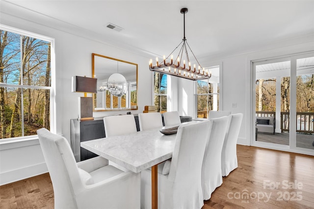 dining space with an inviting chandelier, visible vents, wood finished floors, and a wealth of natural light