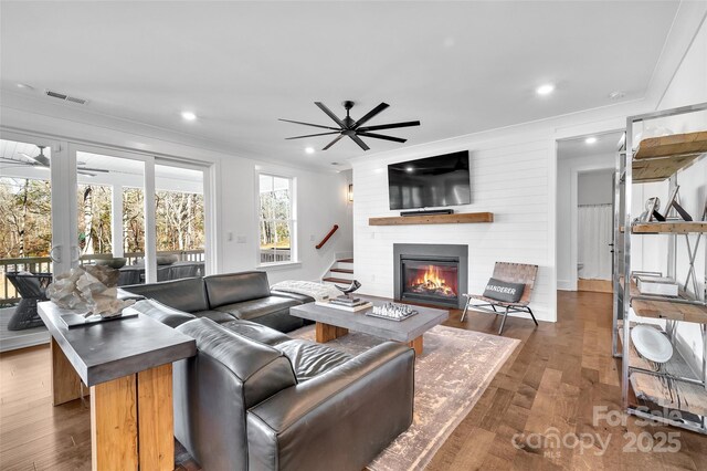 living area featuring crown molding, a large fireplace, a ceiling fan, and visible vents