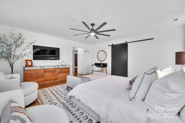 bedroom with visible vents, a barn door, ceiling fan, and wood finished floors