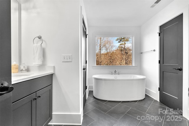 bathroom with visible vents, a freestanding tub, baseboards, and vanity