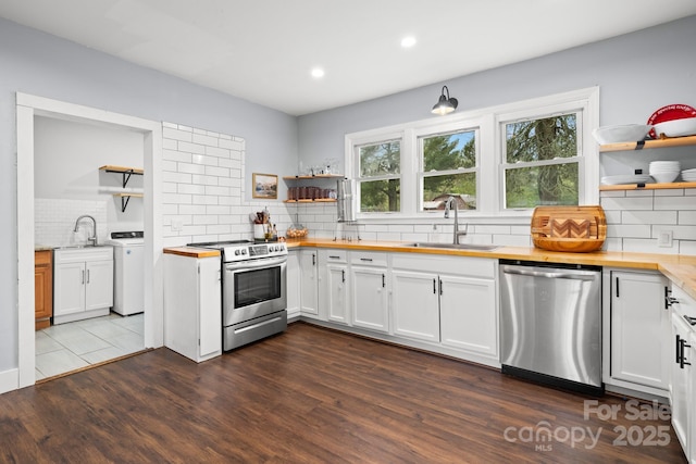 kitchen with independent washer and dryer, open shelves, a sink, wooden counters, and stainless steel appliances