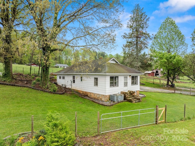 exterior space featuring a lawn, fence, roof with shingles, and central air condition unit