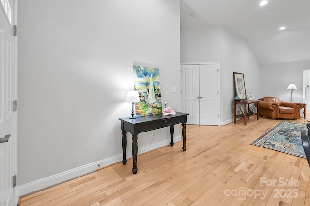 interior space featuring light wood-style floors, baseboards, and high vaulted ceiling