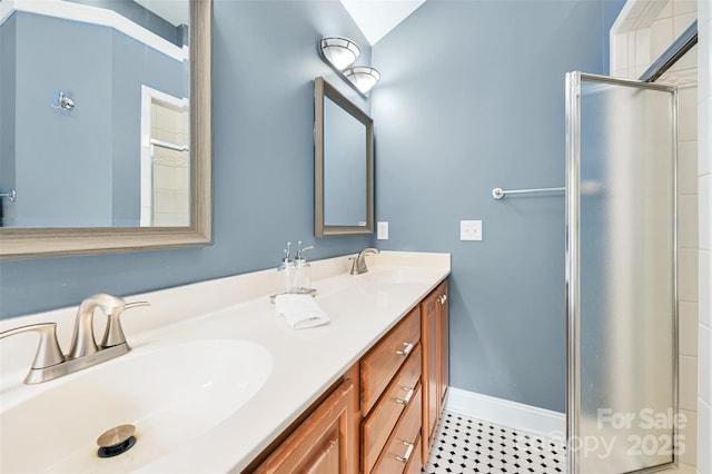 full bathroom with double vanity, baseboards, a shower stall, and a sink