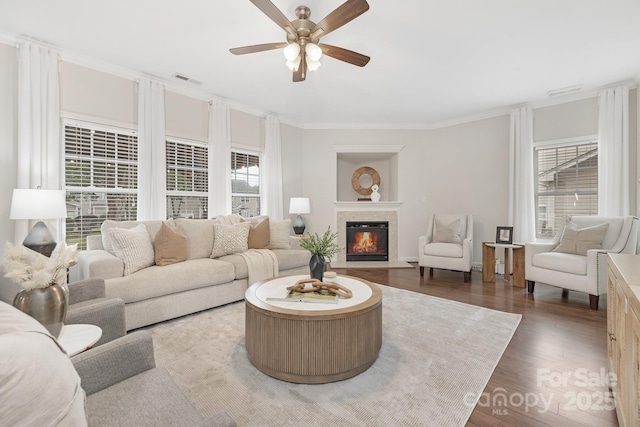 living room with dark wood-style floors, a fireplace with flush hearth, ceiling fan, visible vents, and ornamental molding