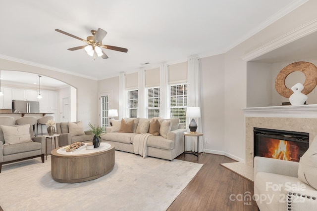 living room with wood finished floors, a ceiling fan, ornamental molding, and arched walkways