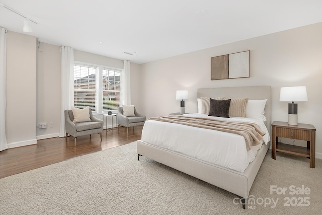 bedroom featuring baseboards, visible vents, wood finished floors, and rail lighting