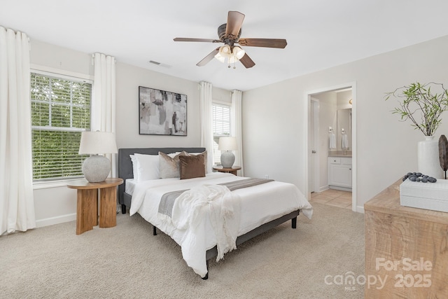 bedroom featuring ensuite bath, a ceiling fan, visible vents, baseboards, and light colored carpet