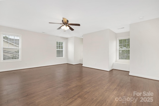 empty room featuring dark wood-style floors, a ceiling fan, a healthy amount of sunlight, and baseboards