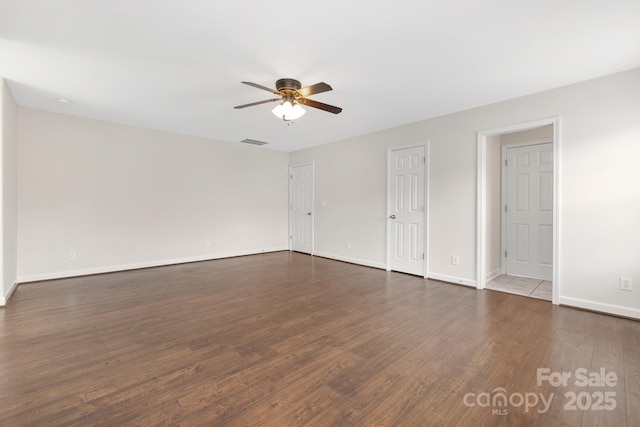 empty room with dark wood-style floors, baseboards, visible vents, and a ceiling fan