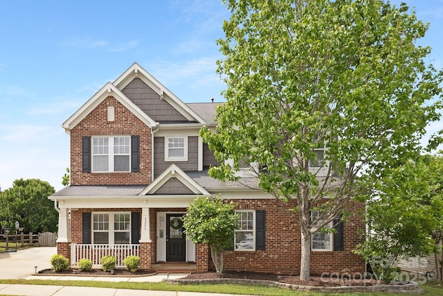 craftsman-style house featuring brick siding, a porch, fence, and roof with shingles