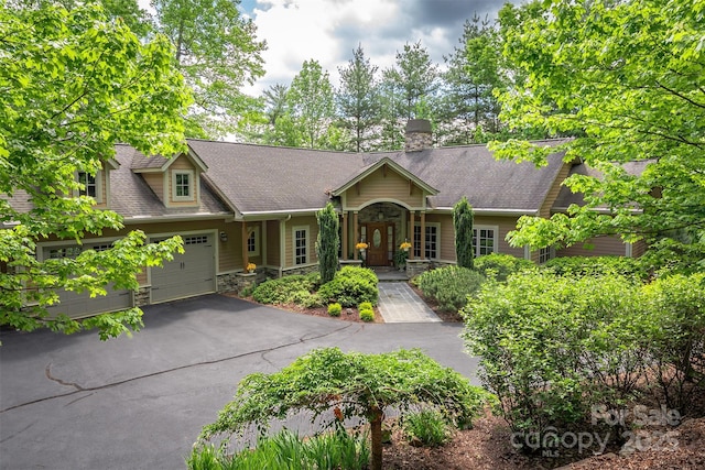 168 Chattooga Run, Hendersonville, NC 28739 - view of front of house featuring stone siding, asphalt driveway, a garage, a chimney, and a shingled roof