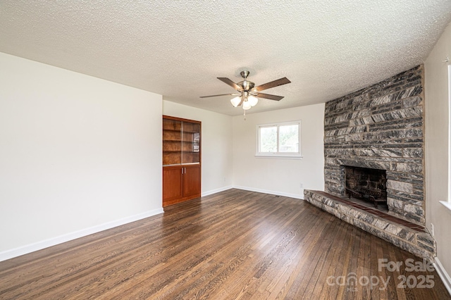unfurnished living room featuring wood finished floors, a stone fireplace, baseboards, ceiling fan, and a textured ceiling