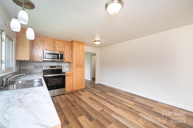 kitchen with light wood-type flooring, light countertops, tasteful backsplash, a sink, and appliances with stainless steel finishes