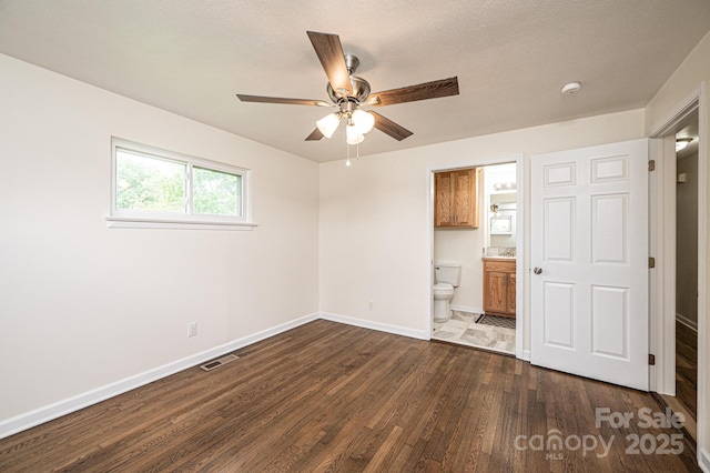unfurnished bedroom with ceiling fan, visible vents, baseboards, ensuite bath, and dark wood-type flooring