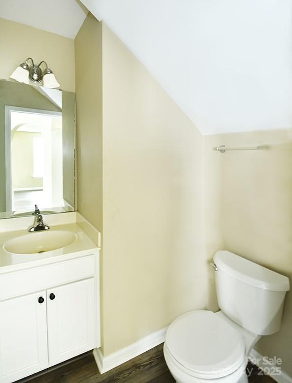 half bath with wood finished floors, toilet, vanity, baseboards, and lofted ceiling