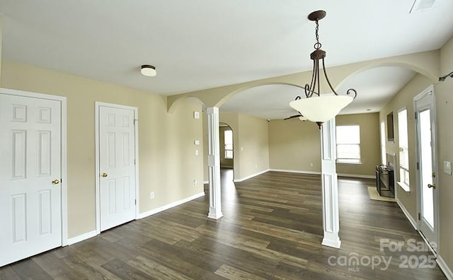 unfurnished dining area featuring arched walkways, dark wood-style flooring, and plenty of natural light